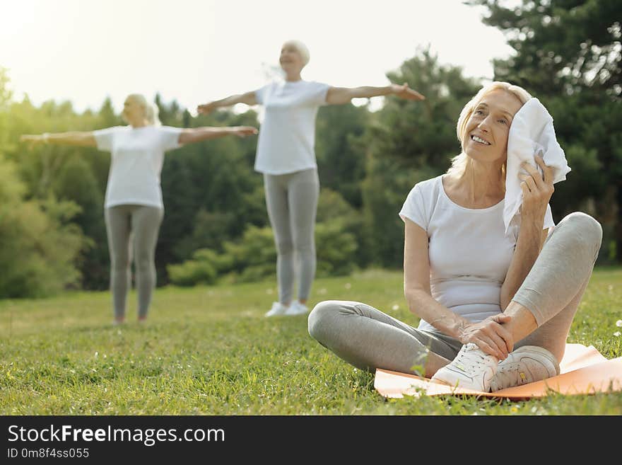 Recharging my batteries. Joyful retired women smiling and wiping her forehead with a towel after taking class in a group training session. Recharging my batteries. Joyful retired women smiling and wiping her forehead with a towel after taking class in a group training session.