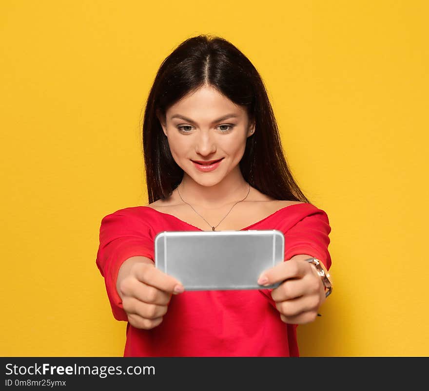 Attractive young woman taking selfie on color background