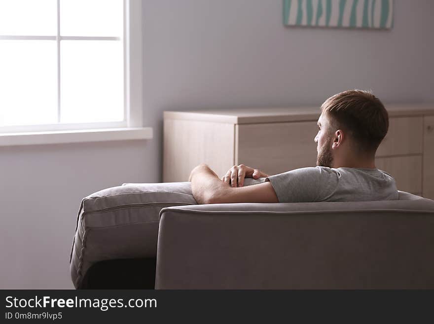 Depressed young man sitting in armchair at home