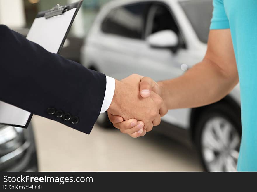 Customer and salesman shaking hands in car salon