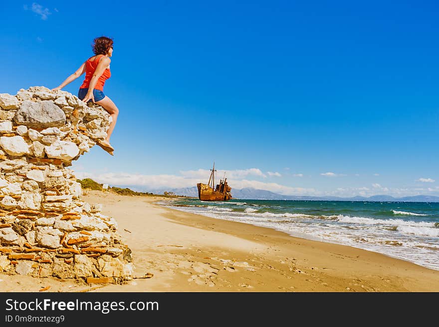 Travel freedom. Mature tourist woman on beach enjoying summer vacation. An old abandoned shipwreck, wrecked boat in the background. Travel freedom. Mature tourist woman on beach enjoying summer vacation. An old abandoned shipwreck, wrecked boat in the background