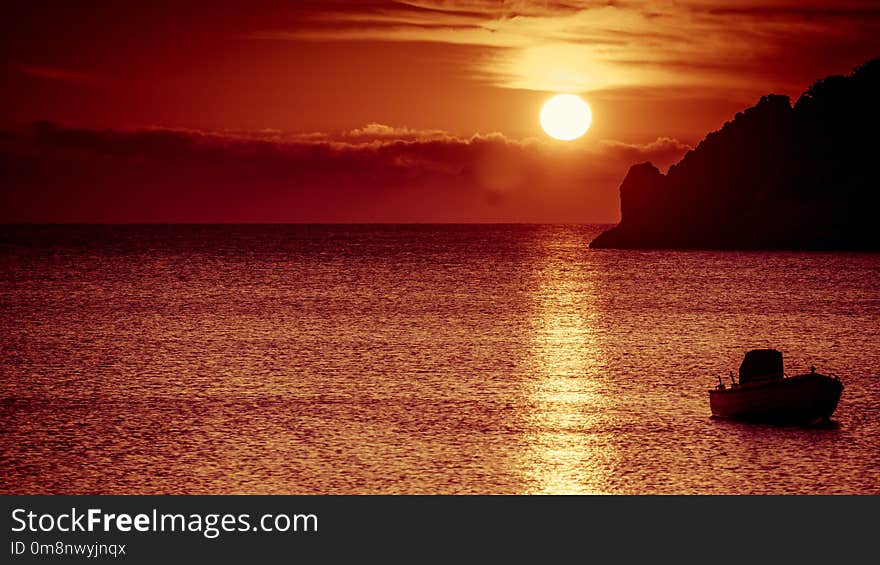 Scenic sunrise or sunset over sea surface, boat anchored in bay, Greece