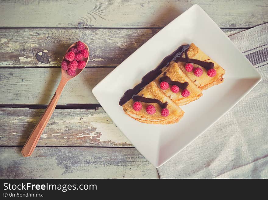 Crepes with fresh raspberries and chocolate syrop on aged wooden background. Top view. Crepes with fresh raspberries and chocolate syrop on aged wooden background. Top view.