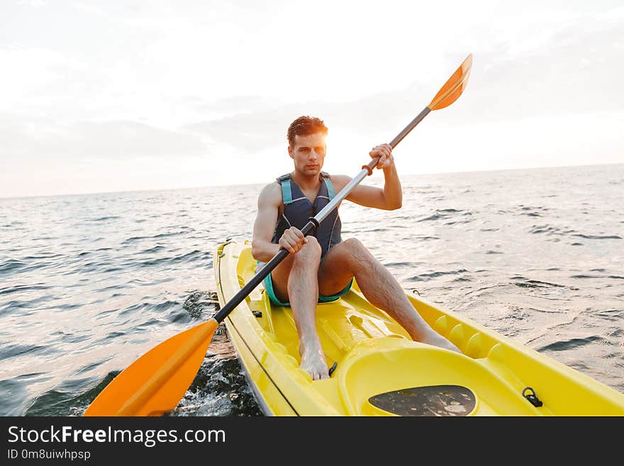 Image of young handsome man kayaking on lake sea in boat.