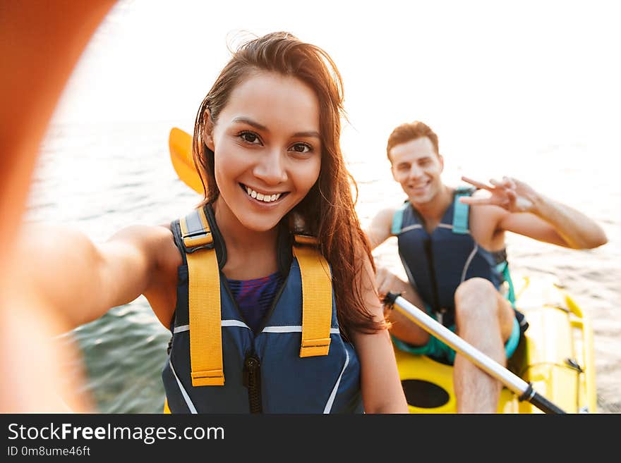 Image of young cute loving couple kayaking on lake sea in boat make selfie by camera.