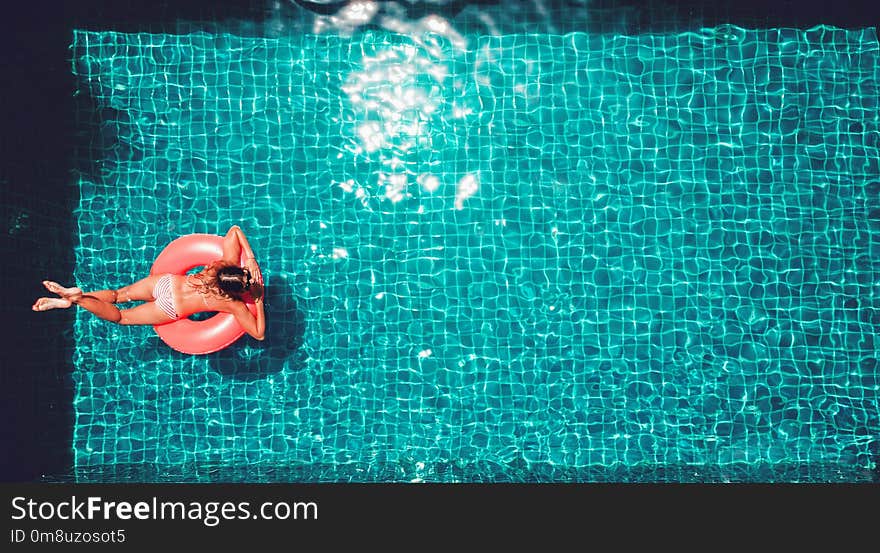 Young pretty slim woman in straw hat on a pink air mattress in t