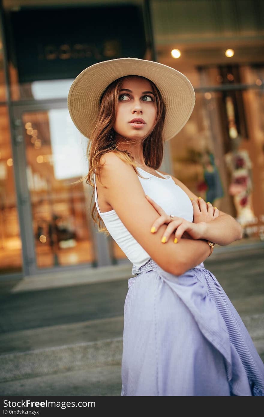 Young woman in hat stands at city street on background of building. Young woman in hat stands at city street on background of building.