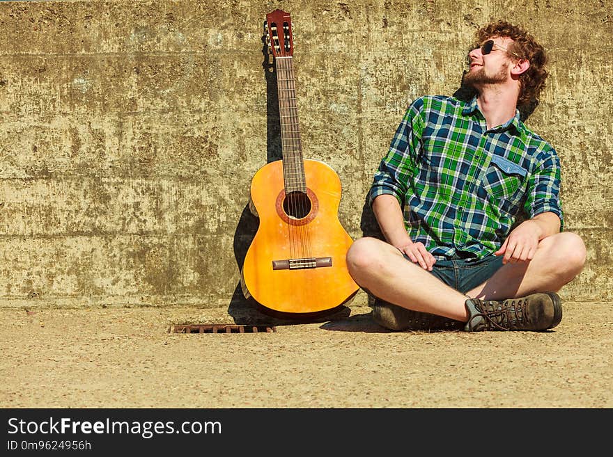 Music and people concept. Young bearded hipster man with guitar outdoor on street