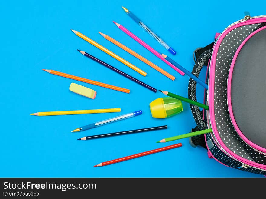 A lot of colored pencils and a school bag on light blue background. The view from the top.