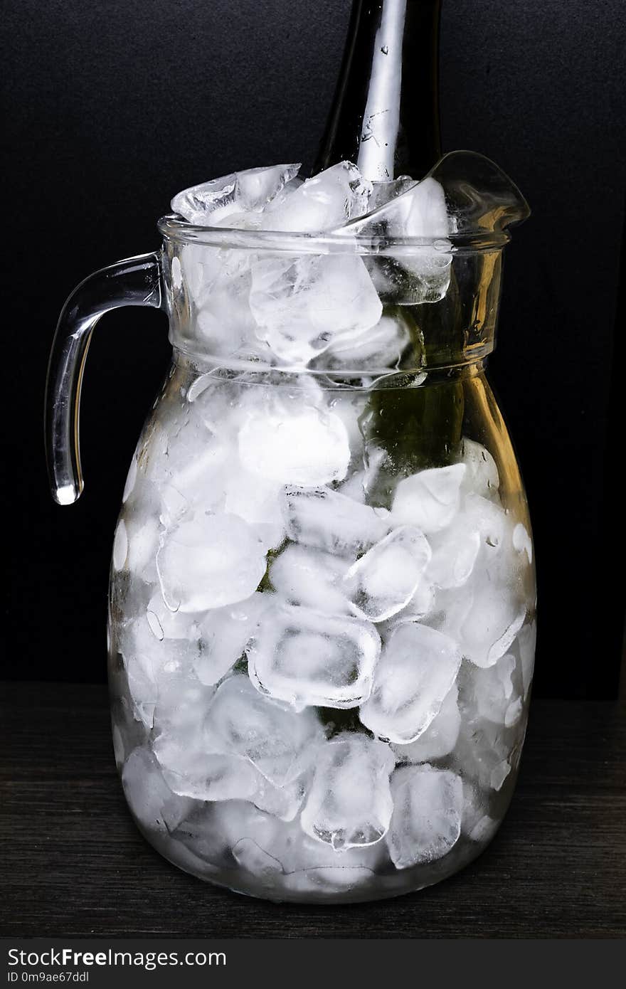 Wine or champagne bottle in glass pitcher with ice isolated on black background