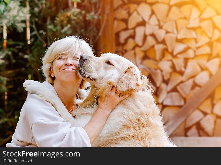 Pretty blonde woman playing with her white dog golden retriever outside, near firewood. Pretty blonde woman playing with her white dog golden retriever outside, near firewood