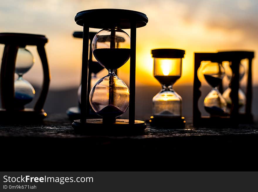 Hourglass Passing of Time Lapse Clouds. An hourglass in front of a bright blue sky with puffy white clouds passing. Time concept. Sunset time. Selective focus