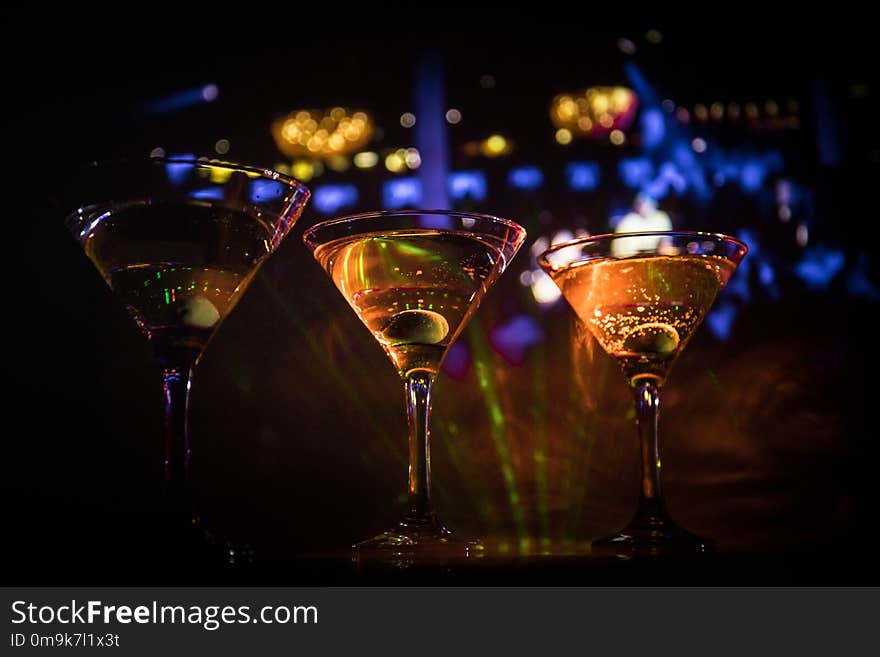 Several glasses of famous cocktail Martini, shot at a bar with dark toned foggy background and disco lights. Club drink concept. Selective focus