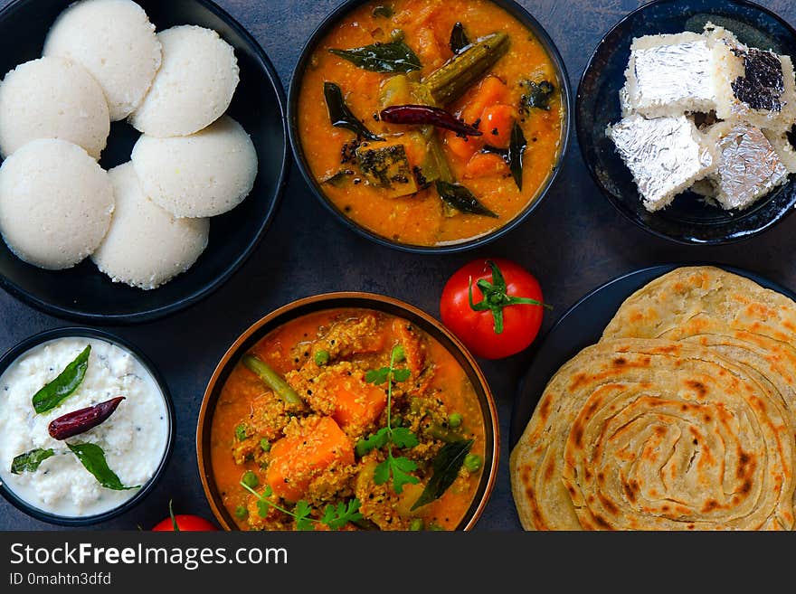 Sourh Indian cuisine consisting of various dishes like idli , sambhar , veg korma, malabar paratha coconut chutney and kalakand dessert. Sourh Indian cuisine consisting of various dishes like idli , sambhar , veg korma, malabar paratha coconut chutney and kalakand dessert