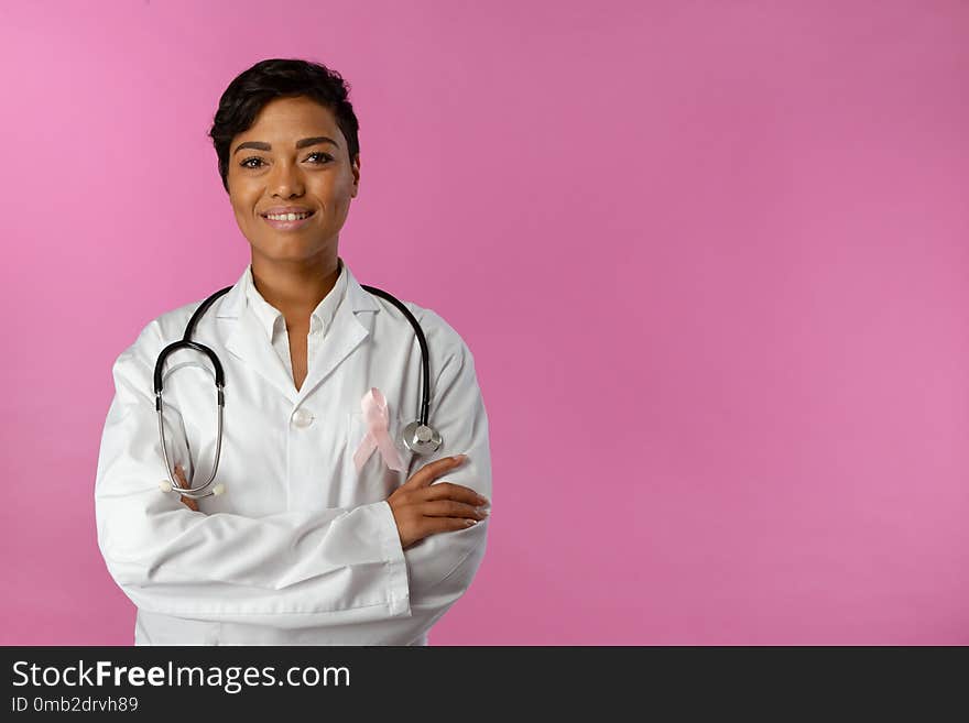 Smiling nurse wearing breast cancer awareness ribbon on pink background