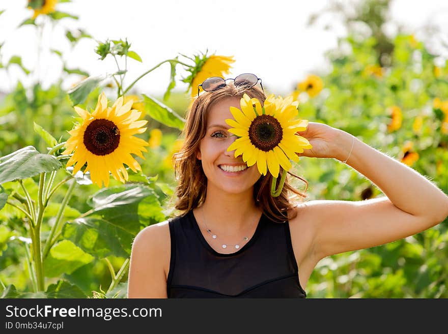 Laughing young woman holds a sunflower in front of her eyes