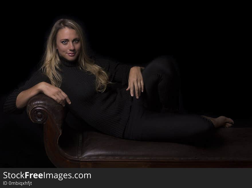 Beautiful woman portrait in low light sitting on a brown leather sofa