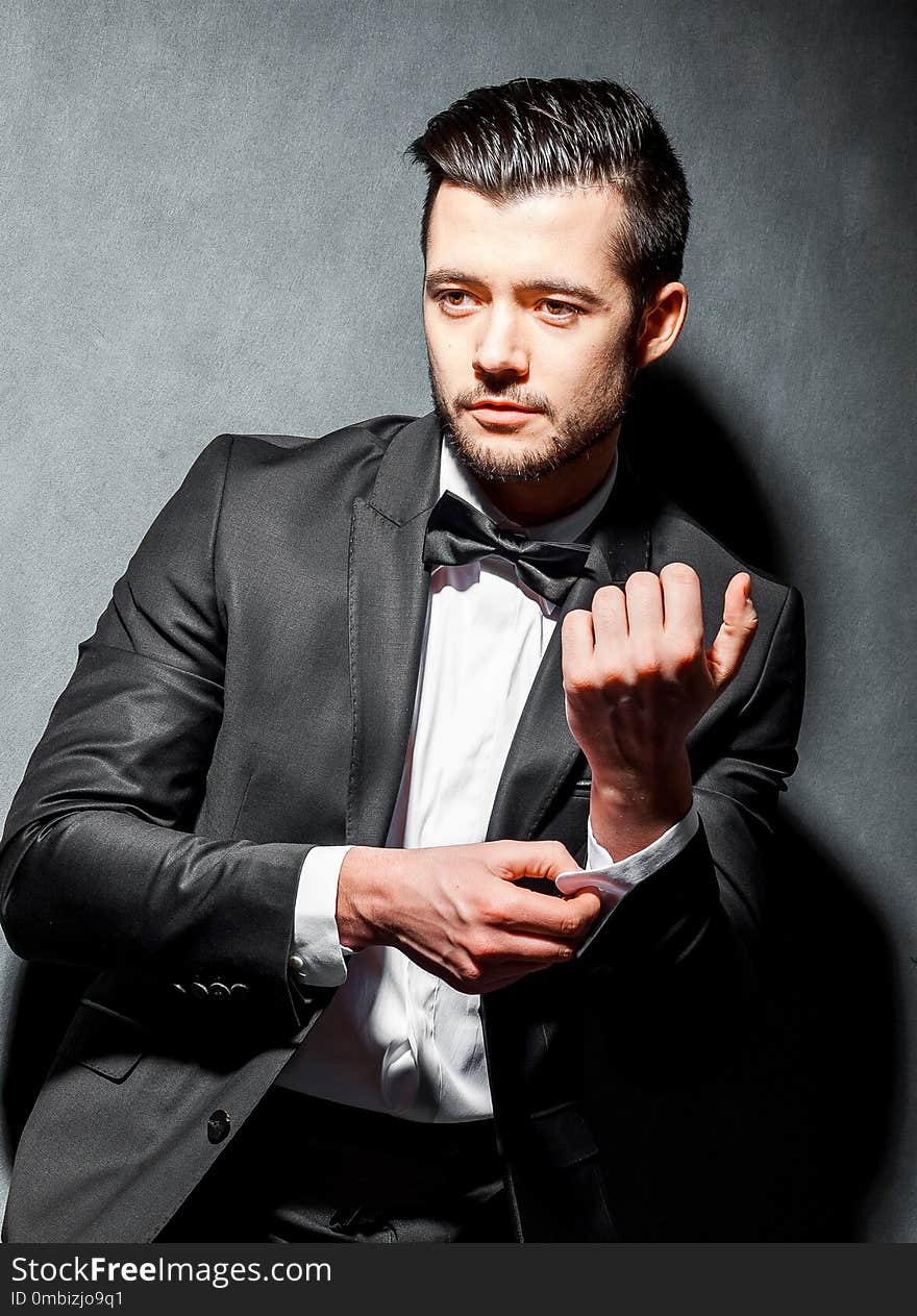 Portrait of confident handsome man in black suit with bowtie posing in dark studio background