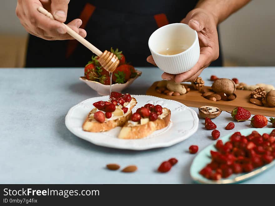 Chef cook prepares Italian bruschetta pours honey with strawberries, cheese, camembert, brie, cooking by chef hand. Authentic lifestyle image.