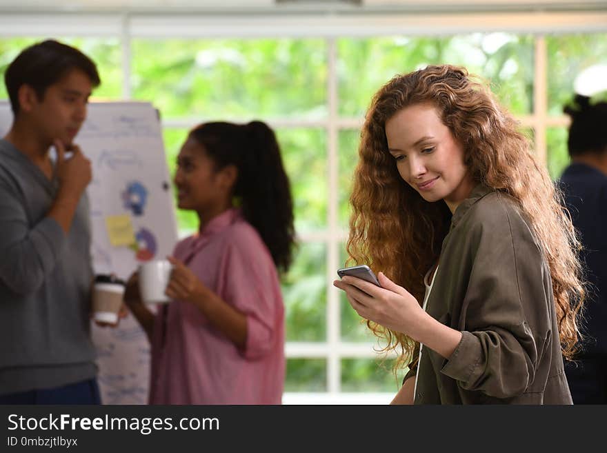 Young business woman using smartphone in the office with colleagues in the background