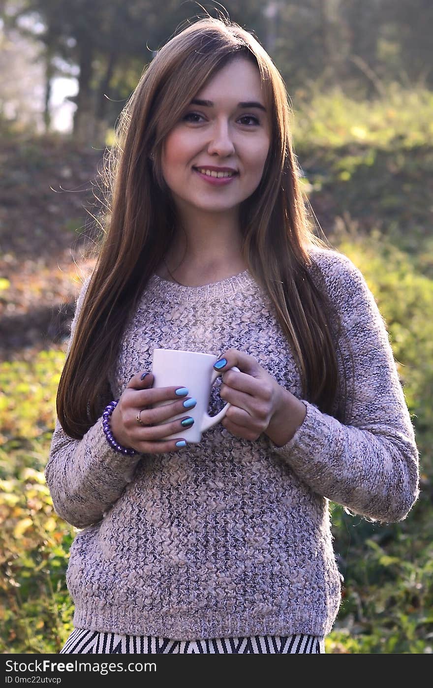 Portrait of a cheerful young smiling woman in autumn forest holding ceramic white coffee cup in autumn forest outdoors. Portrait of a cheerful young smiling woman in autumn forest holding ceramic white coffee cup in autumn forest outdoors