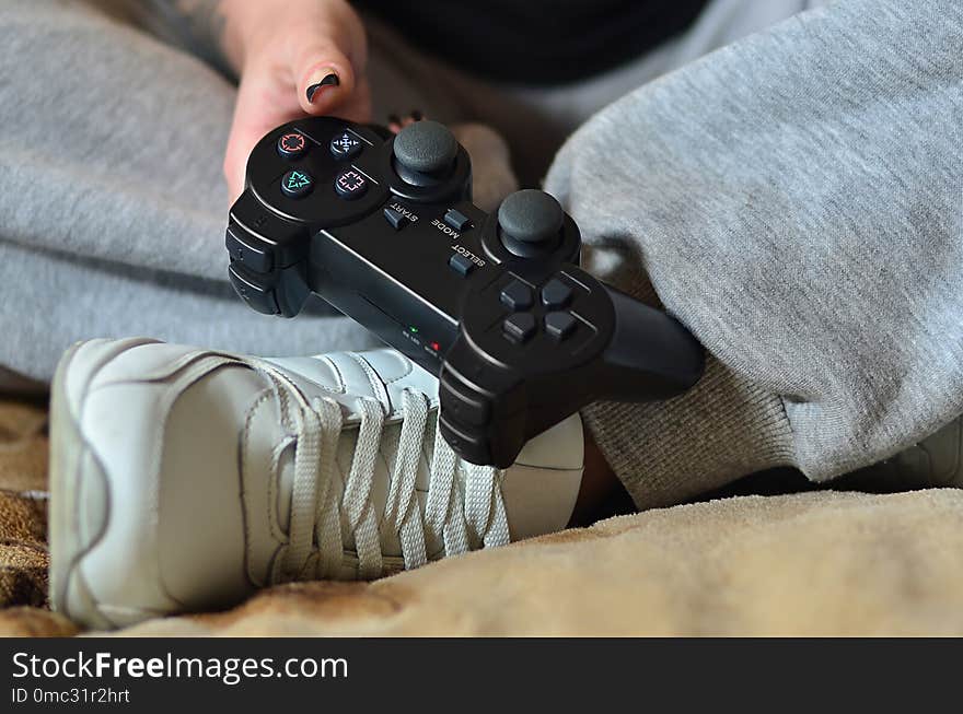 A young girl in gray pants holds a black modern game joystick with a lot of buttons for managing video games. The concept of youth leisure through video games. A young girl in gray pants holds a black modern game joystick with a lot of buttons for managing video games. The concept of youth leisure through video games