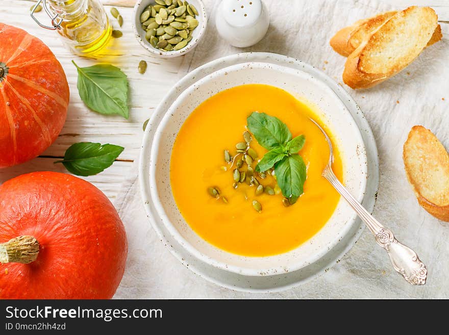 Dietary vegetarian pumpkin cream soup puree with olive oil, seeds and Basil on a light wooden table in a white plate. Selective focus