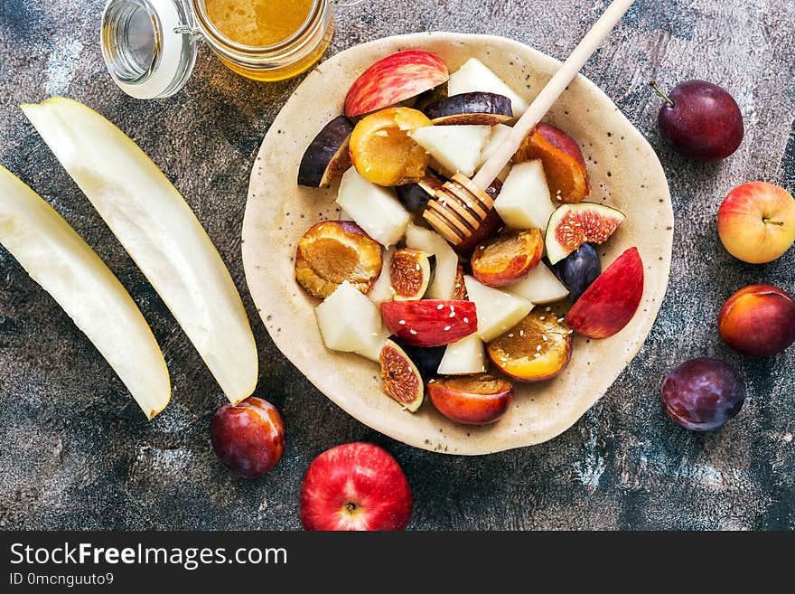 Fresh fruit salad of melon, figs, apples, plums and honey on a dark rustic background, top view. The concept of healthy eating. flat lay