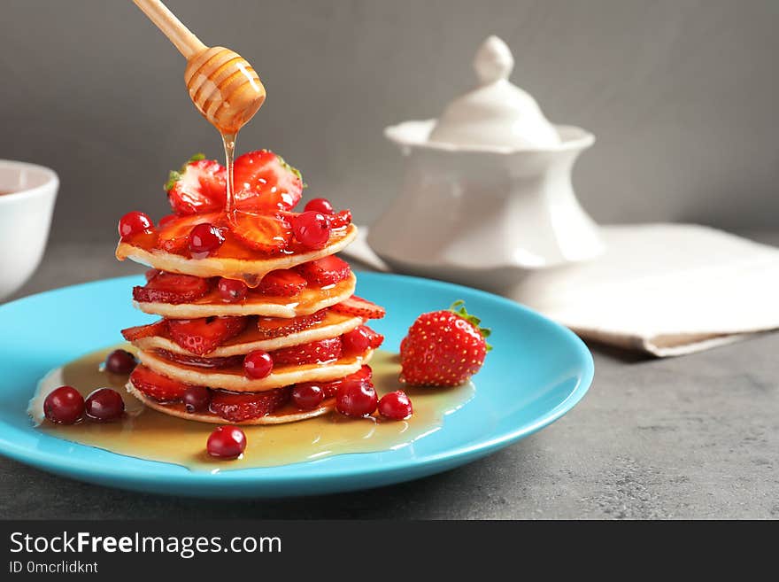 Pouring honey onto tasty pancakes with berries on plate