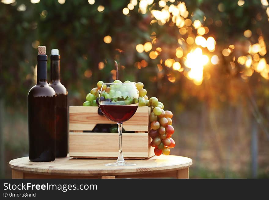 Bottles and glass of red wine with fresh grapes on wooden table