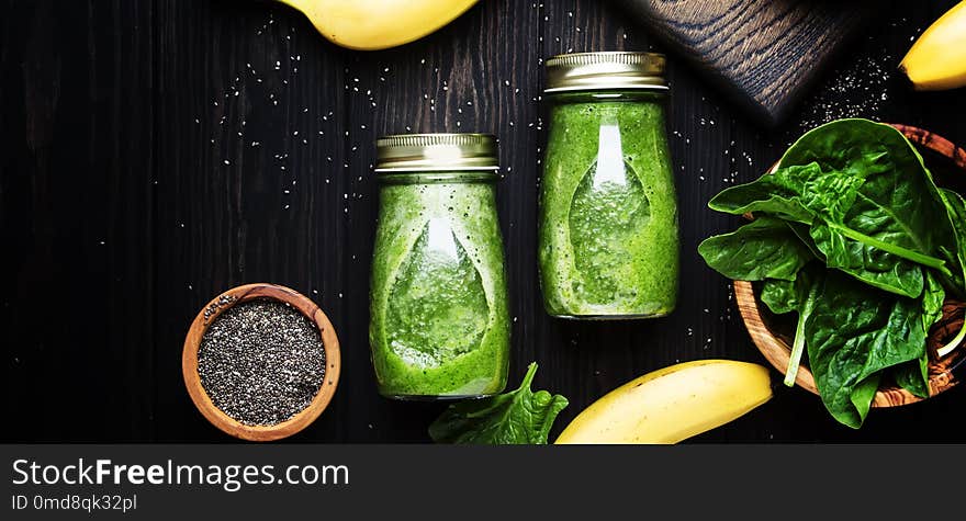 Incredibly useful green spinach smoothies in glass bottles with chia on wooden background with yellow bananas, top view