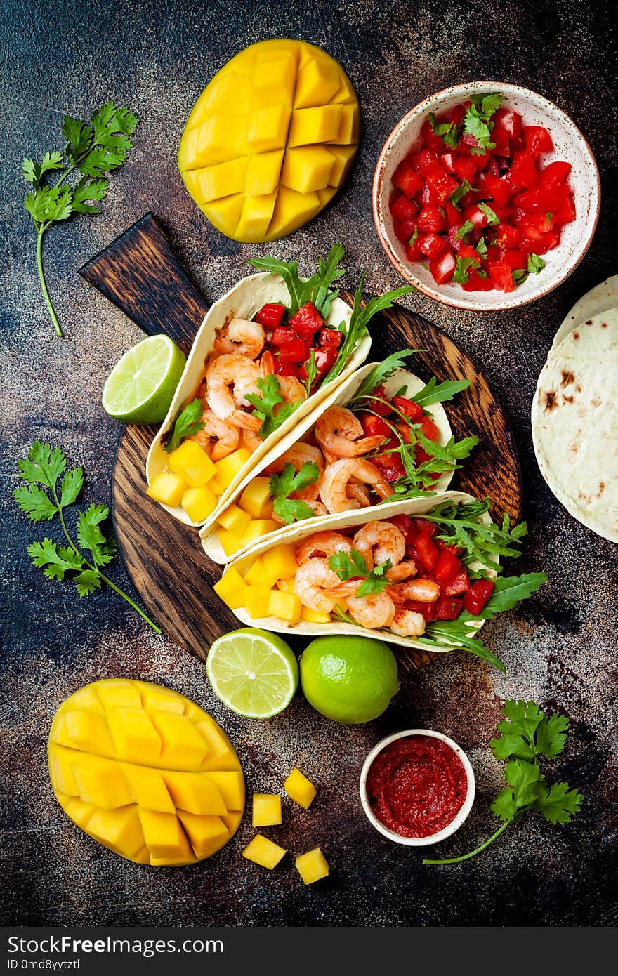 Mexican shrimp tacos with avocado, tomato, mango salsa on rustic stone table. Recipe for Cinco de Mayo party. Top view, overhead, flat lay.