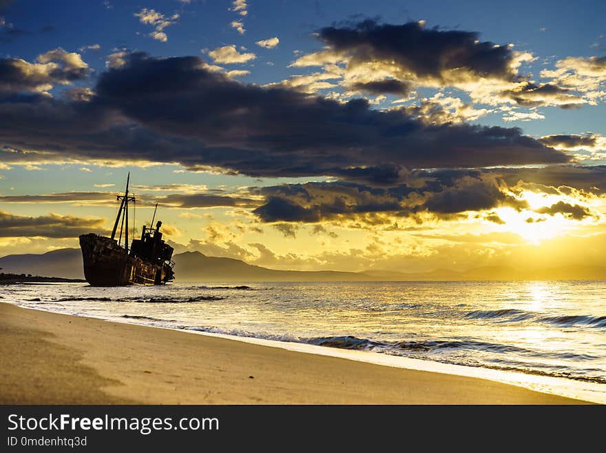 An old abandoned shipwreck, wrecked boat sunken ship stand on beach coast. Scenic sunset sky. An old abandoned shipwreck, wrecked boat sunken ship stand on beach coast. Scenic sunset sky