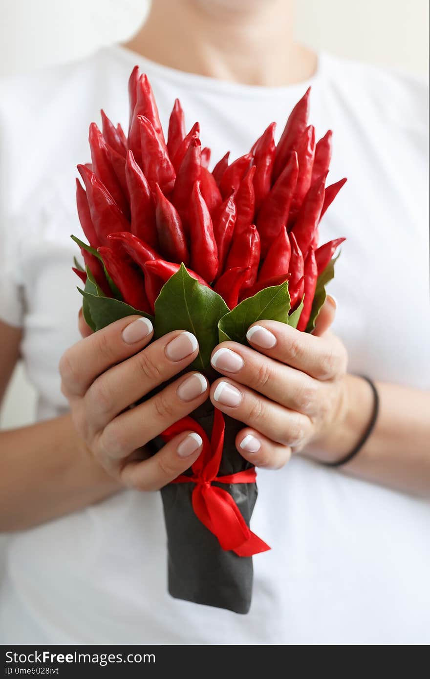 Woman is holding a small bouquet made of red hot peppers in the form of a heart.