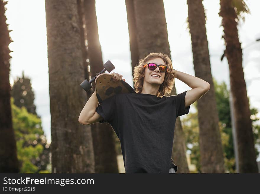 Stylish young blond curly hair man holding skateboard on shoulders and smile. Stylish young blond curly hair man holding skateboard on shoulders and smile