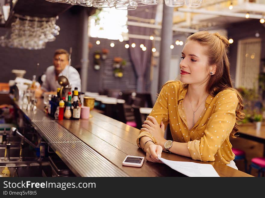 Relaxing alone. Calm beautiful young girl kindly smiling and looking at the professional barman while sitting opposite him. Relaxing alone. Calm beautiful young girl kindly smiling and looking at the professional barman while sitting opposite him