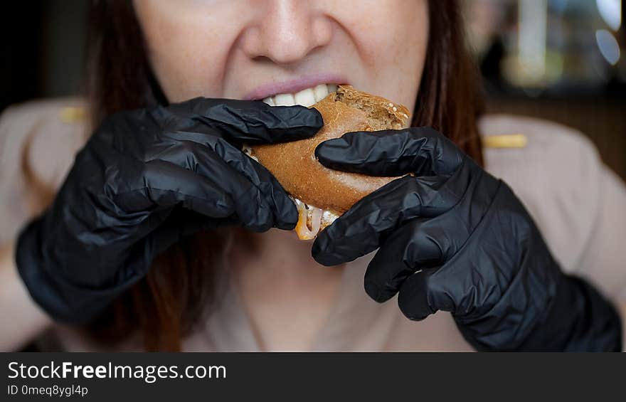 Close up of pretty girl in black gloves eating a hamburger in cafe