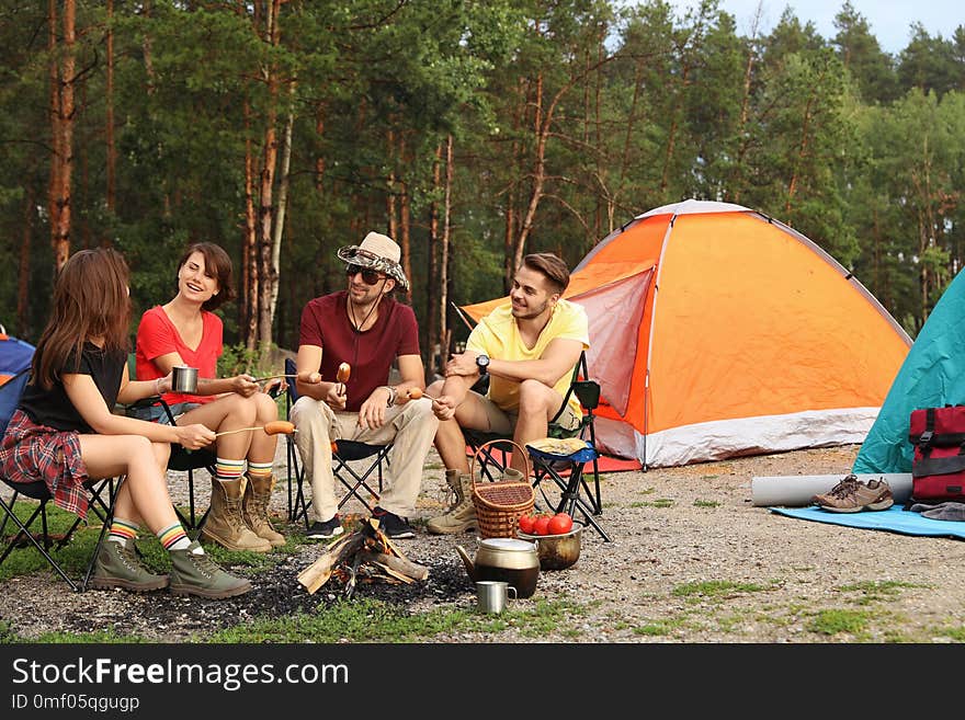 People having lunch with sausages near camping tent outdoors