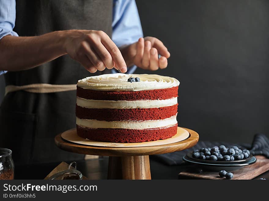 Woman decorating delicious homemade red velvet cake with blueberries at table