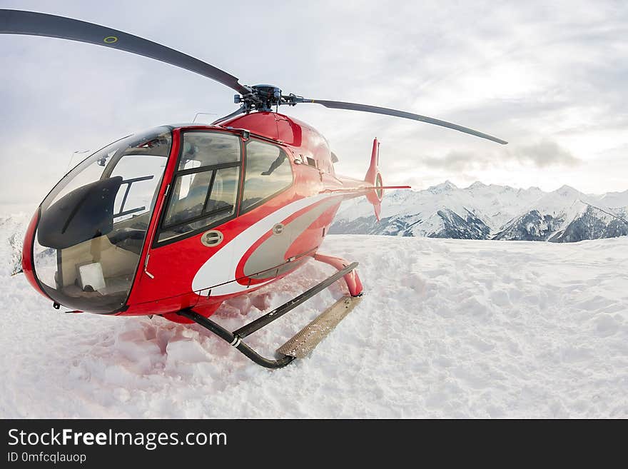 Red rescue helicopter lands standing in snowy mountains.