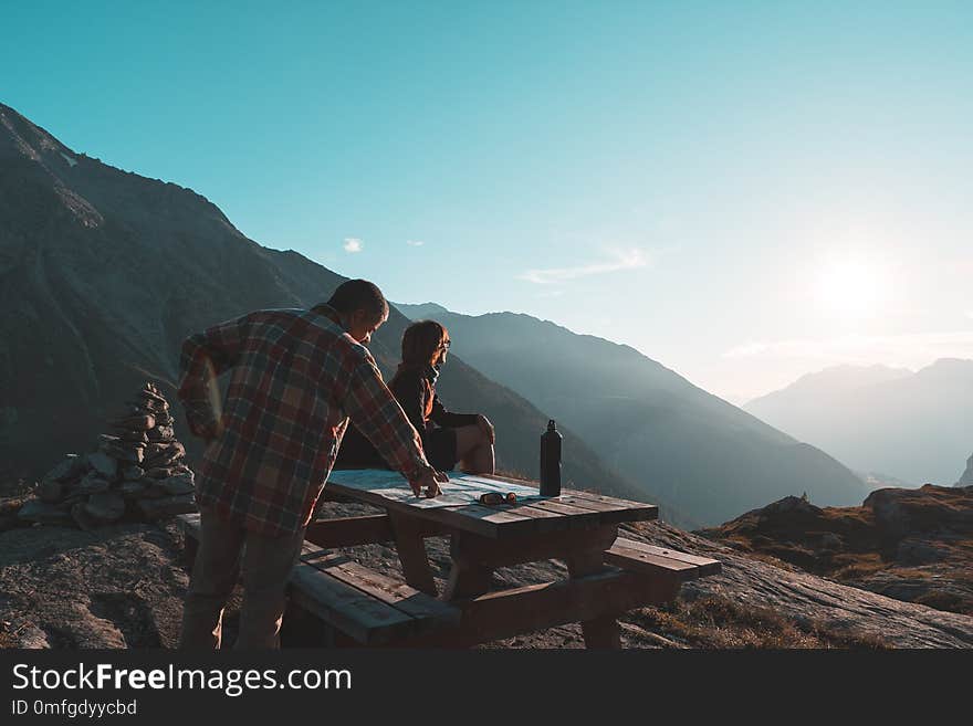 Coouple hikers reading trekking map on table in backlight, rear view. Adventure exploration on the Alps.