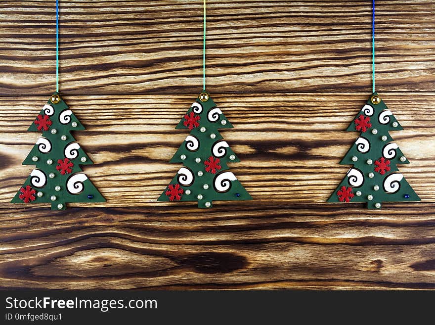 Three toy green fir trees with decorative ornaments on a wooden background.