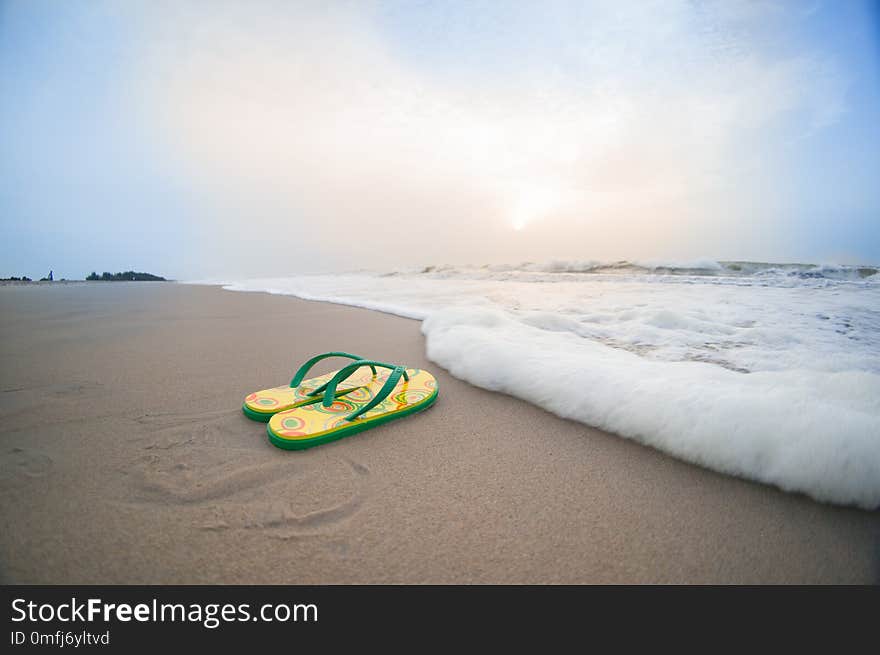 Yellow colorful flip flops lying on beach in pondicherry chennai tamil nadu with brown sand, surf, waves and cloudy skies. Perfect vacation shot to relax, unwind and de stress on a working day. Yellow colorful flip flops lying on beach in pondicherry chennai tamil nadu with brown sand, surf, waves and cloudy skies. Perfect vacation shot to relax, unwind and de stress on a working day