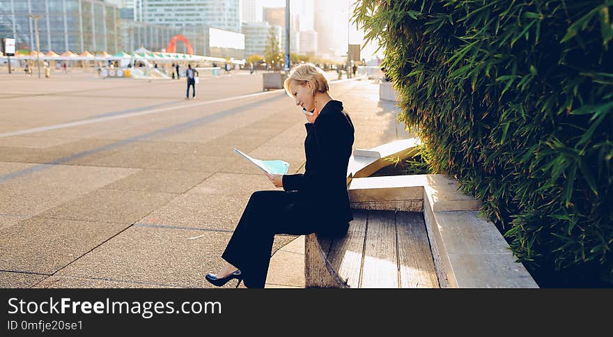 Secretary talking by smartphone with document case in outdoors