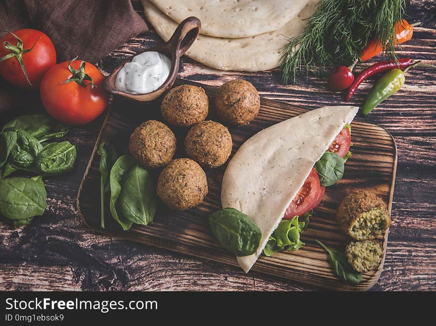 Falafel, fresh vegetables ,sauce and pita bread on wooden table