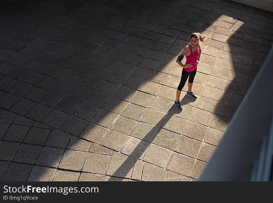 Mature woman taking a break after sport training in city street. Fitness runner relaxing after city jogging and working out outdoors. High angle view of determined runner in sportswear standing on sidewalk with copy space. Mature woman taking a break after sport training in city street. Fitness runner relaxing after city jogging and working out outdoors. High angle view of determined runner in sportswear standing on sidewalk with copy space.