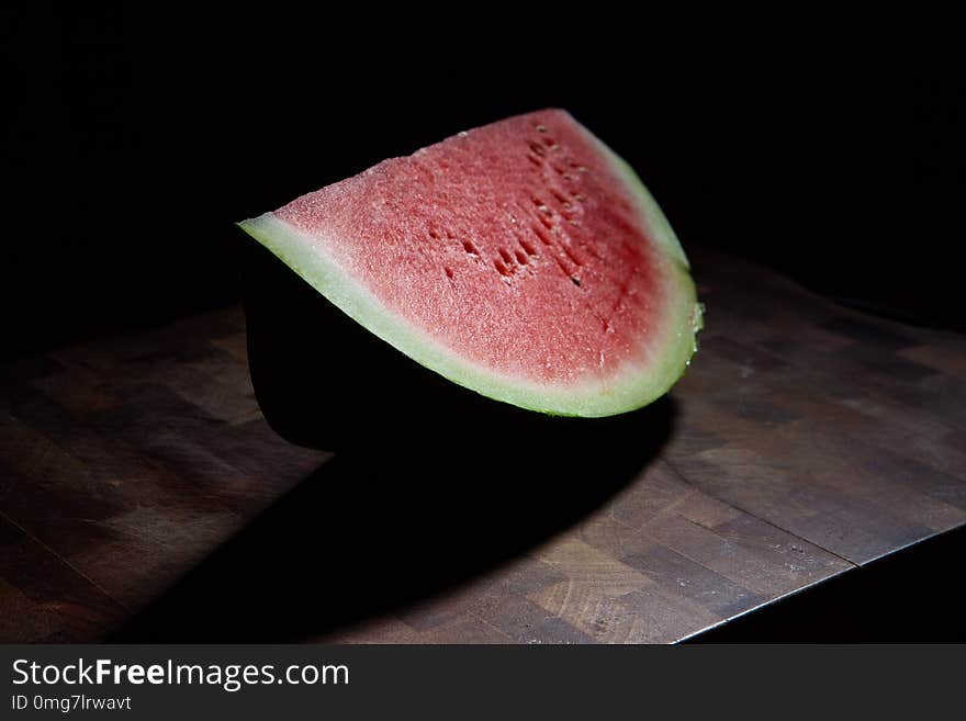 Watermelon slice on chopping board extreme closeup on black background with harsh light. Watermelon slice on chopping board extreme closeup on black background with harsh light