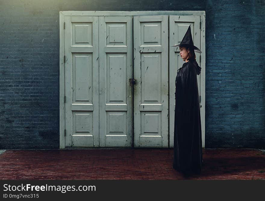 Portrait of woman in black Scary witch halloween costume with Old Brick Wall of the Ancient Castle of the Witch is background Vintage style Color