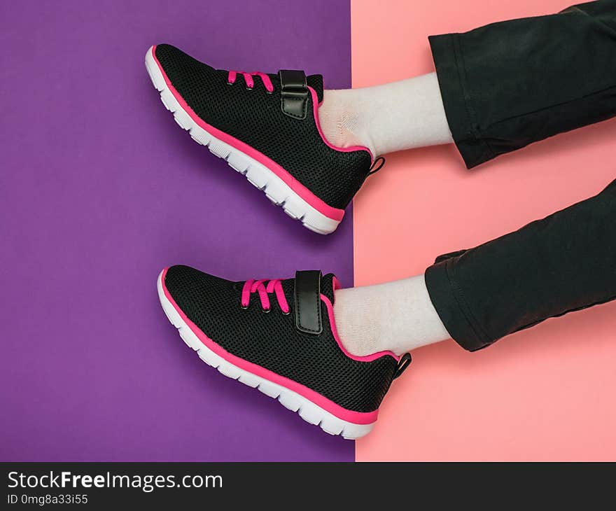 The girl`s legs in sweatpants and bright sneakers on a background of two colors.