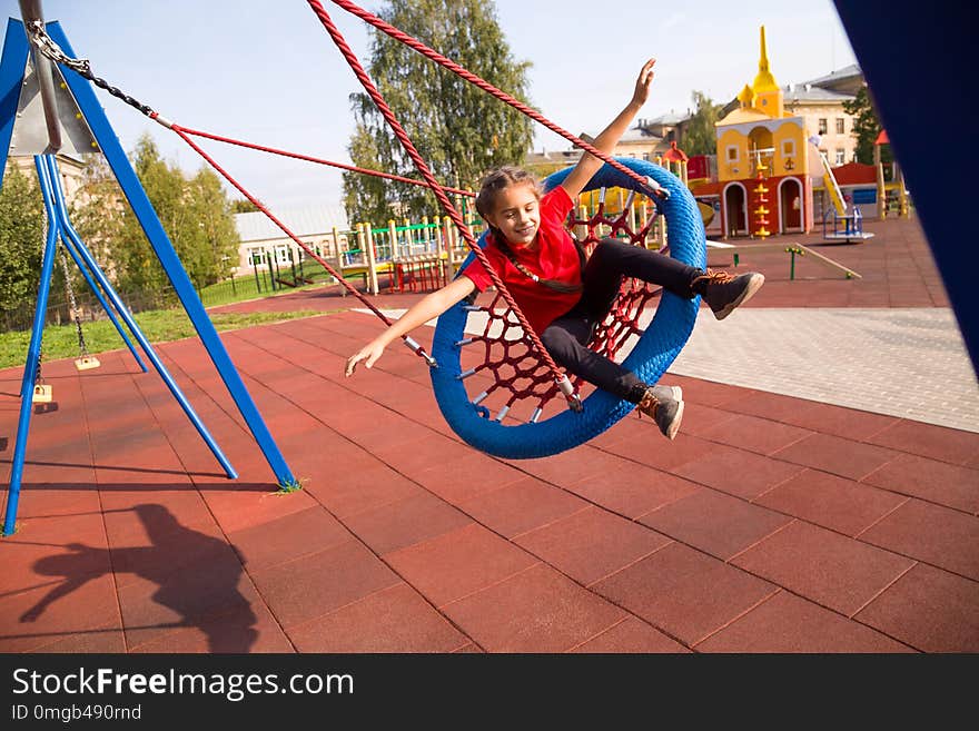 Happy smiling girl swinging on a swing with closed eyes and arms outstretched at playground